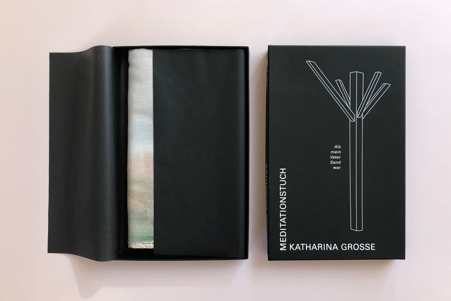 Das Foto zeigt eine schwarze Schachtel, Boden und Deckel mit weißer Schrift. Innen liegt ein Tuch in einem schwarzen Seidenpapier.